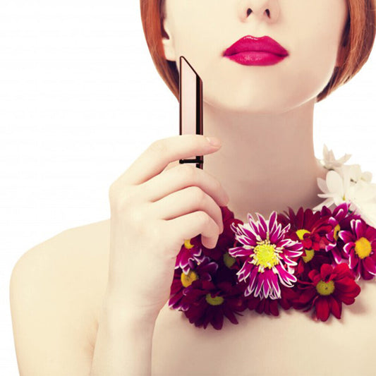A person with red lipstick and a floral necklace holding a gold-colored vibrator.