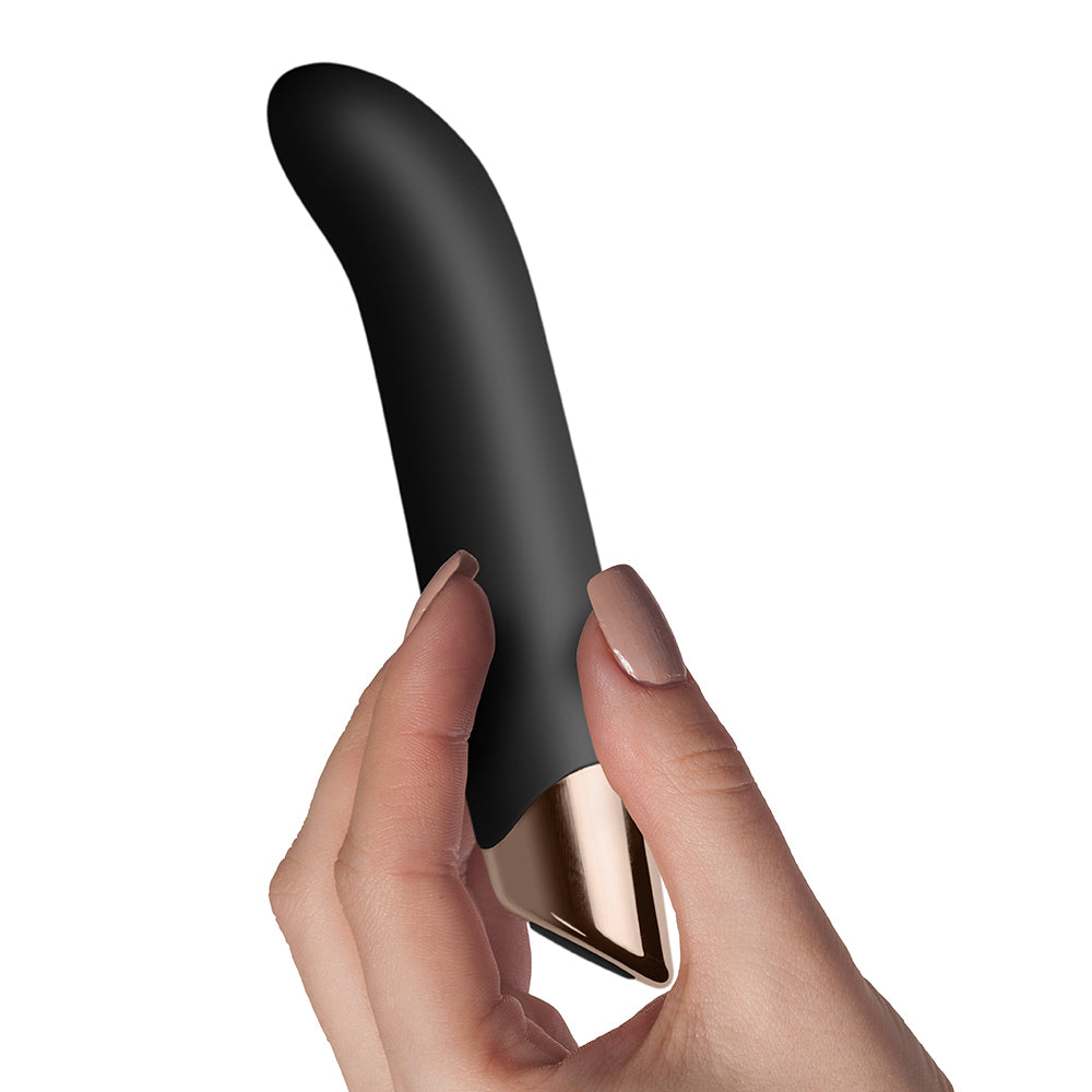 A sleek, black G-spot vibrator with an ergonomic angled tip, resting on a rock, with a branch in the background.