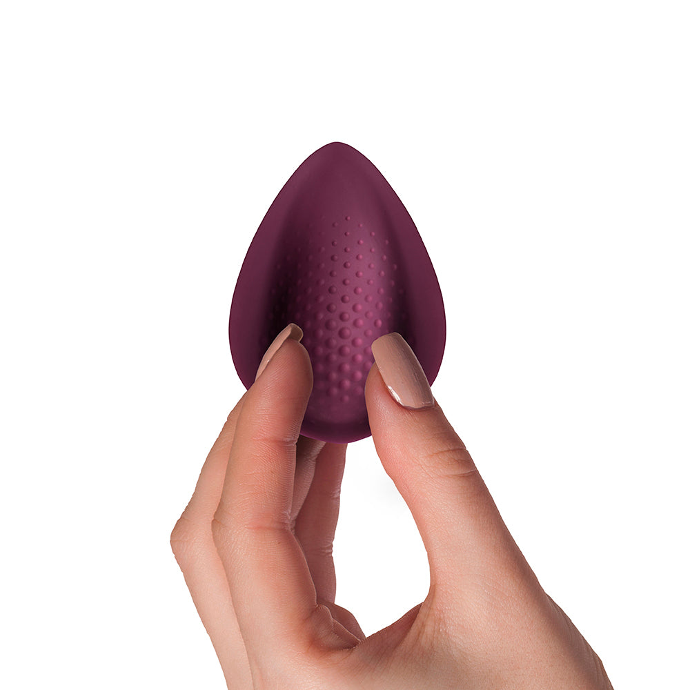 A purple, teardrop-shaped vibrator being held between fingers, with a textured surface and a small remote control attached.