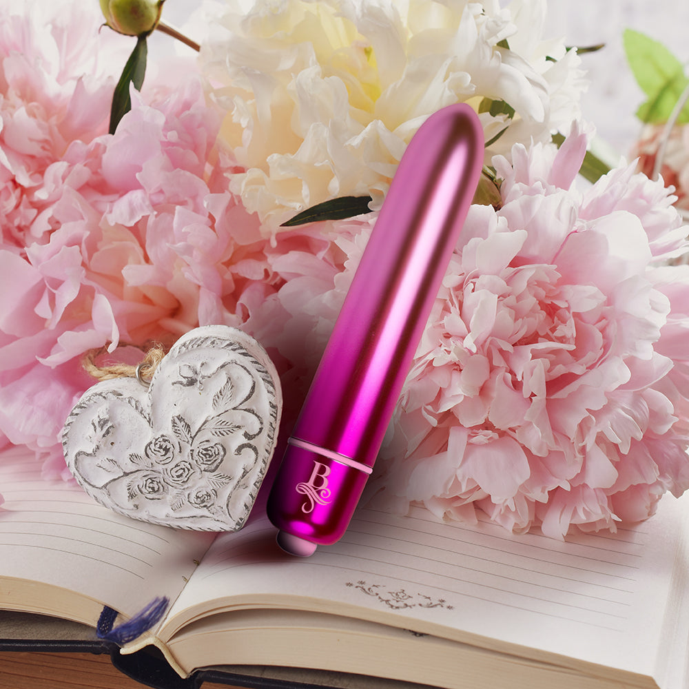 A pink, bullet-shaped vibrator placed on an open journal with a decorative heart-shaped lock and keys, surrounded by pink and white flowers.