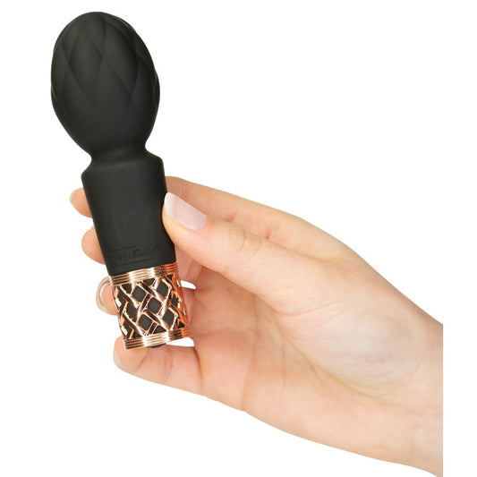 A hand holding a small, black Pillow Talk mini massager with a velvety silicone head and a rose gold-colored base.