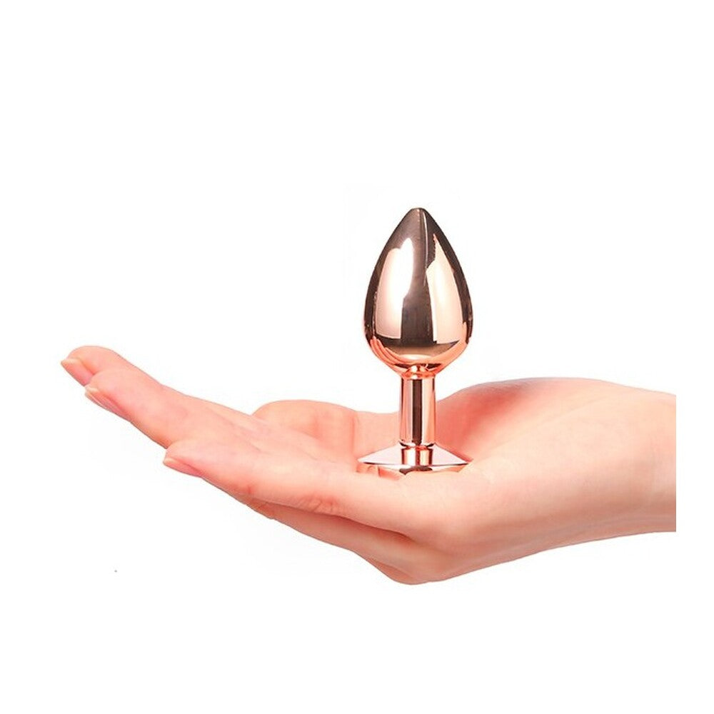 Rose gold anal plug held in a hand against a white background