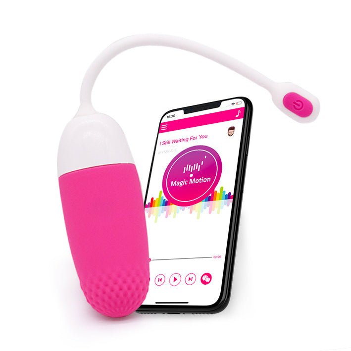 A pink, compact vibrator with a white flexible tail, shown alongside a smartphone displaying the Magic Motion app.
