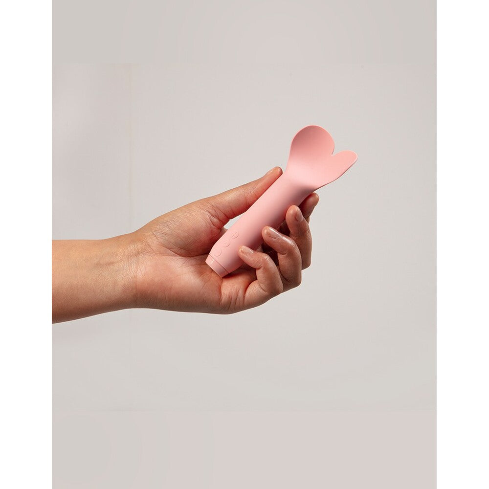 A hand holding a pink, heart-shaped bullet vibrator.