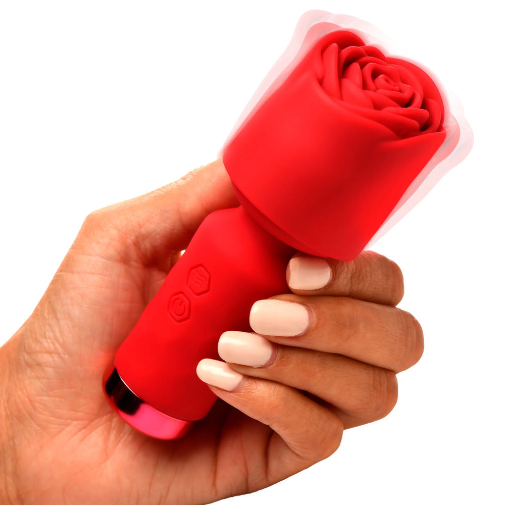 A hand holding a small, red, rose-shaped wand vibrator with a detachable sleeve.