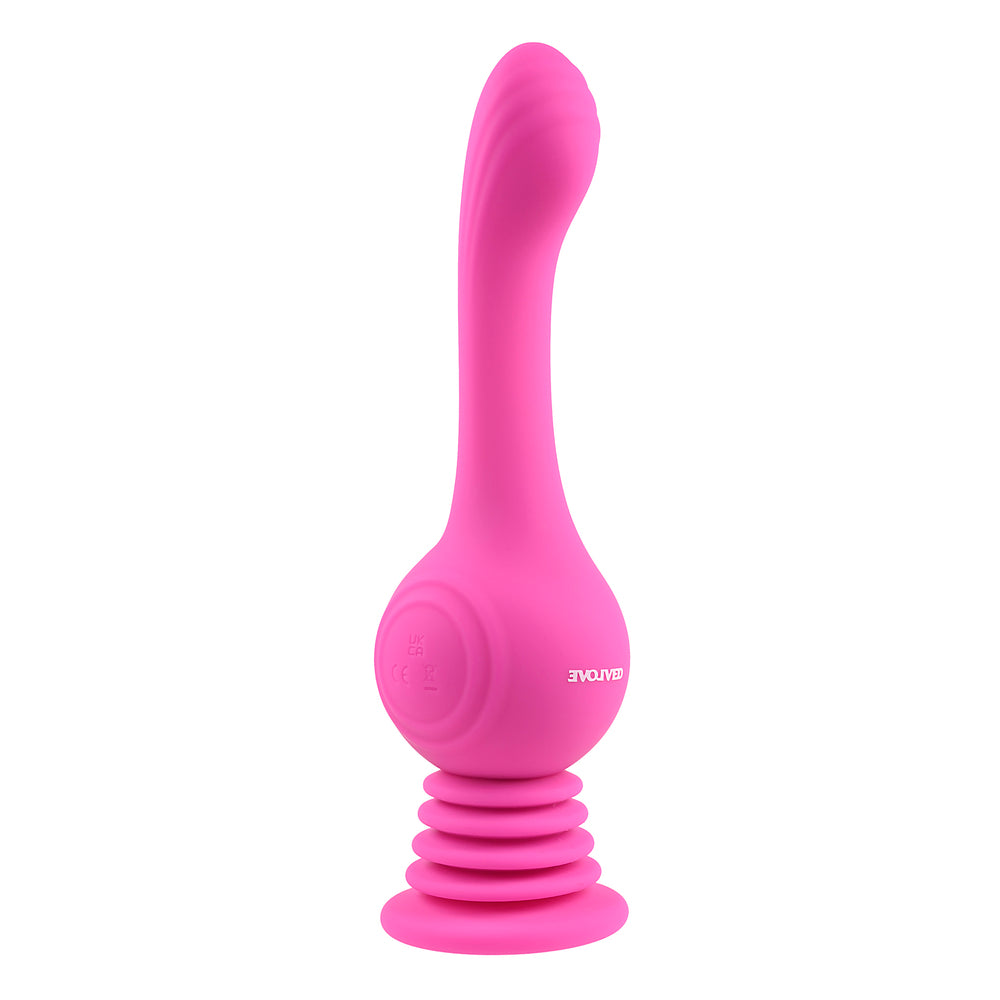 A pink, gyroscopic vibrator with an arched, textured shaft and a accordion-style suction cup base. It stands upright next to a measuring tape, which shows its height, and is accompanied by two sunflowers.