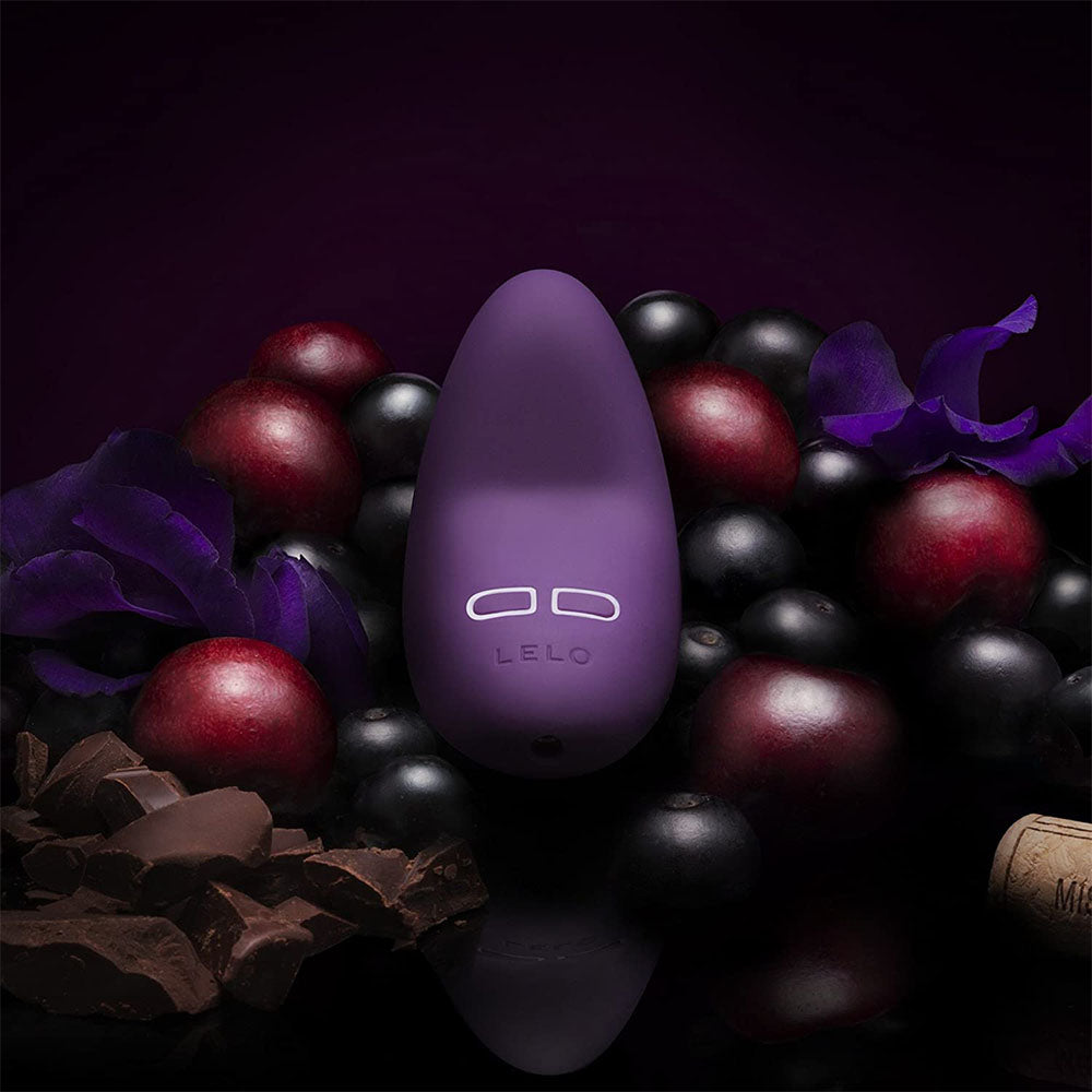 Purple LELO product surrounded by grapes on a dark background