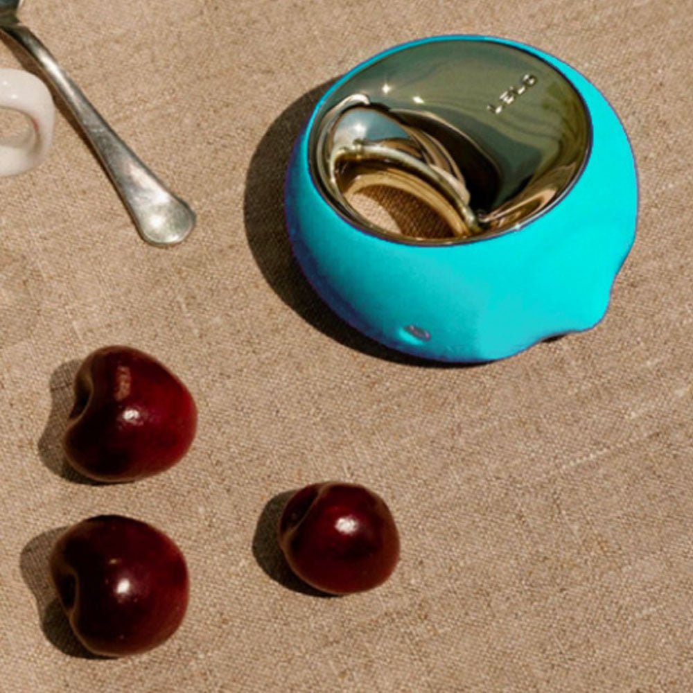 Turquoise bowl with a spoon and cherries on a beige surface