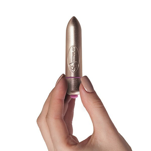A small, gold-colored bullet vibrator being held between fingers, showing its compact size and sleek design.