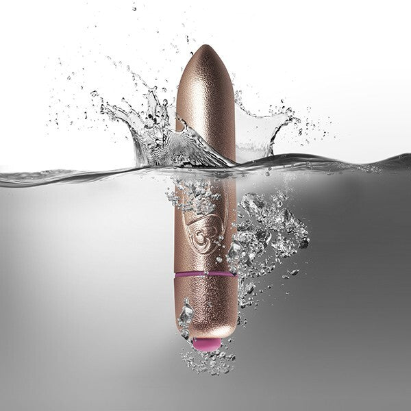 A small, gold-colored bullet vibrator being held between fingers, showing its compact size and sleek design.