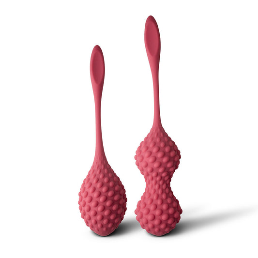 A pair of pink silicone kegels with sensory nodules and retrieval tails, designed for ergonomic insertion and stimulation.