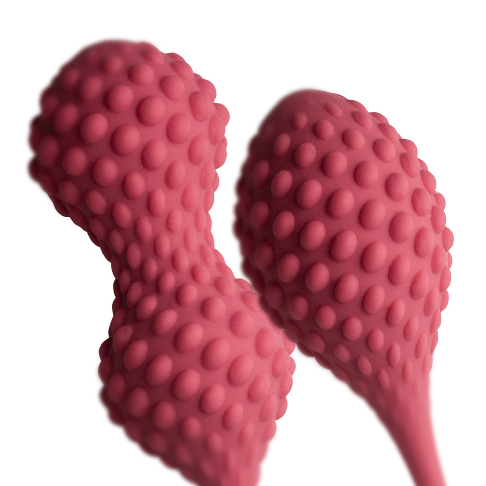 A pair of pink silicone kegels with sensory nodules and retrieval tails, designed for ergonomic insertion and stimulation.