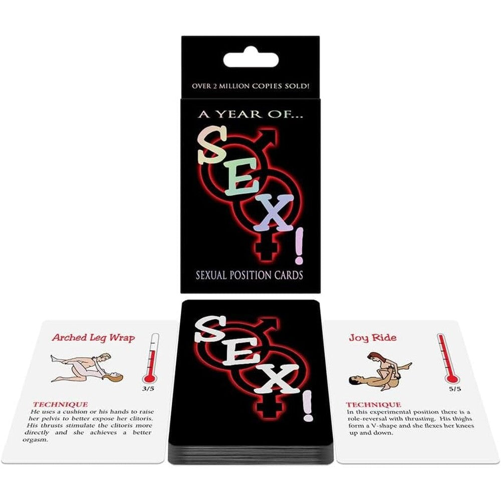 The image shows a card game box titled "A Year of SEX!" along with a few cards displayed in front of the box. The cards depict different sexual positions with illustrations and names like "Arched Leg Wrap" and "Joy Ride.