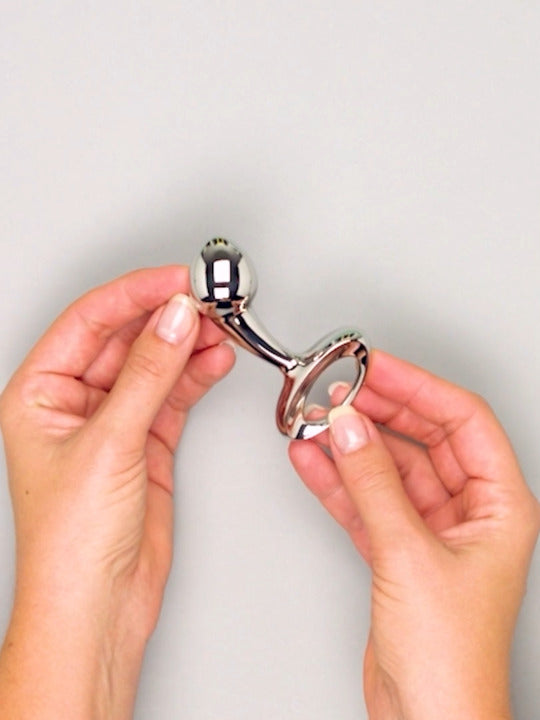 Metallic bottle opener held by hands against a plain background