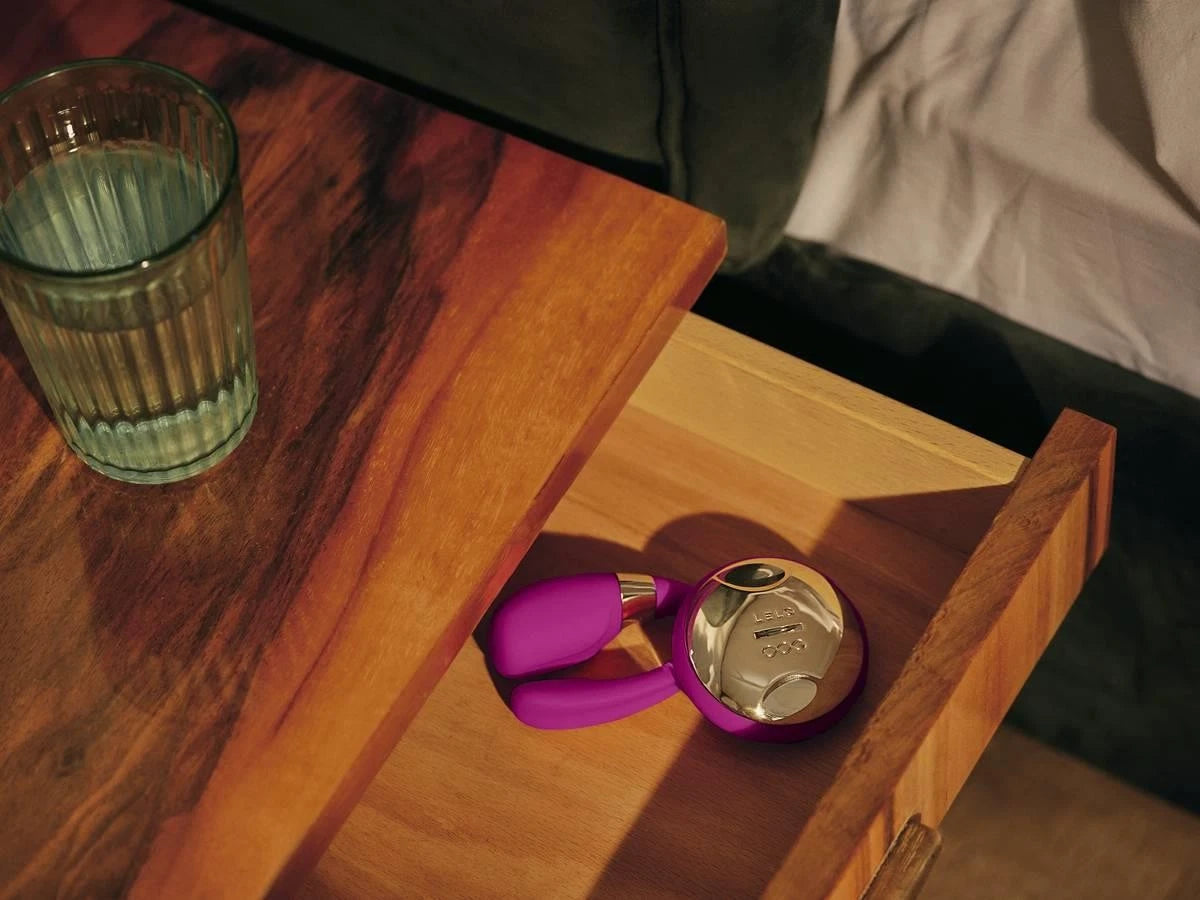Small round mirror with purple frame on a wooden surface next to a glass of water.