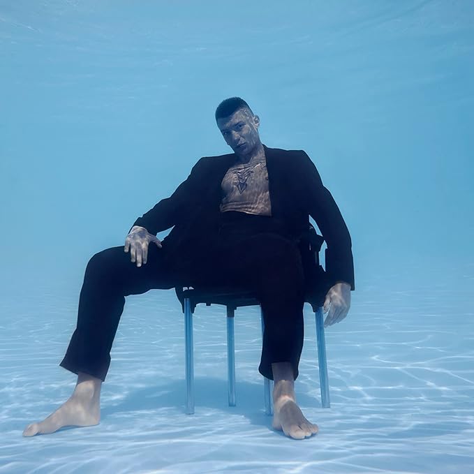 Person sitting on a chair underwater wearing a black suit.