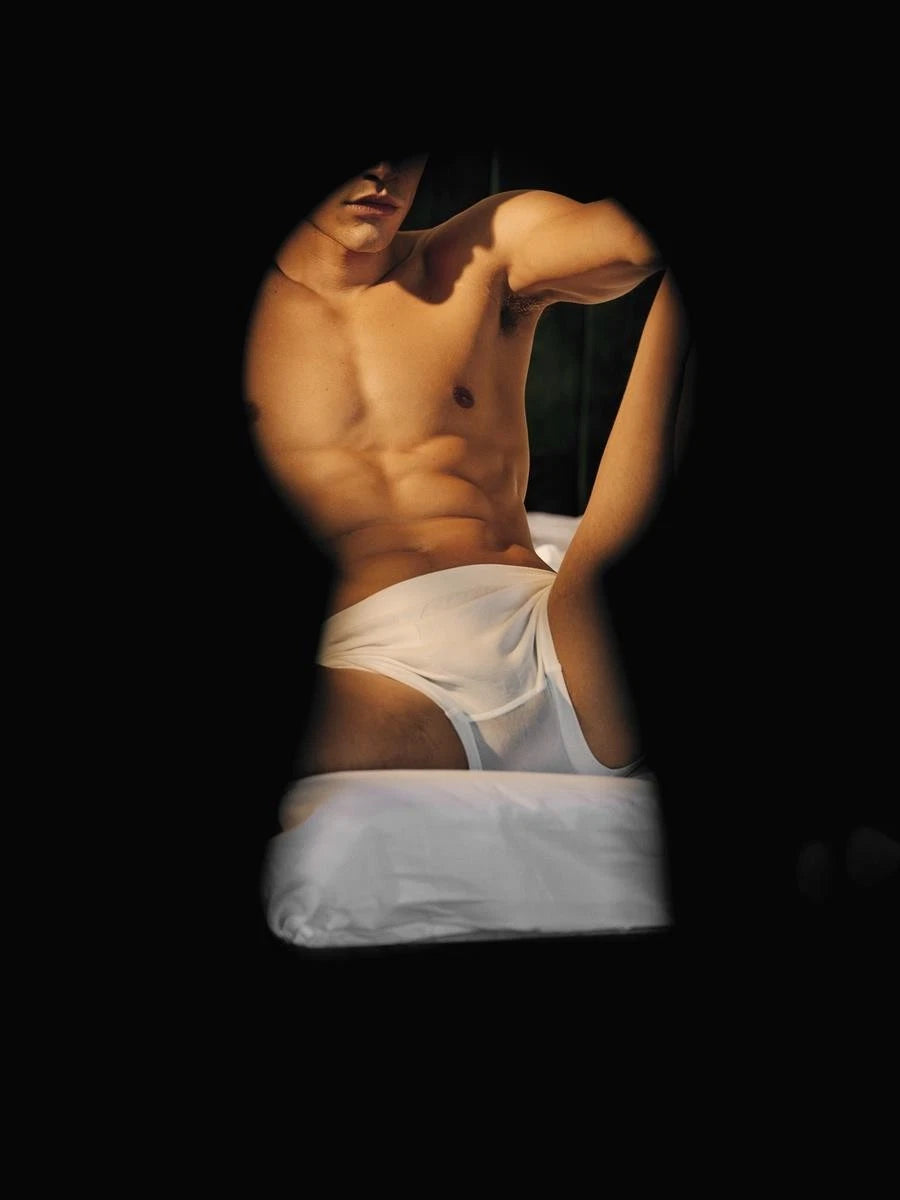 Man in white underwear sitting on a bed with a black background